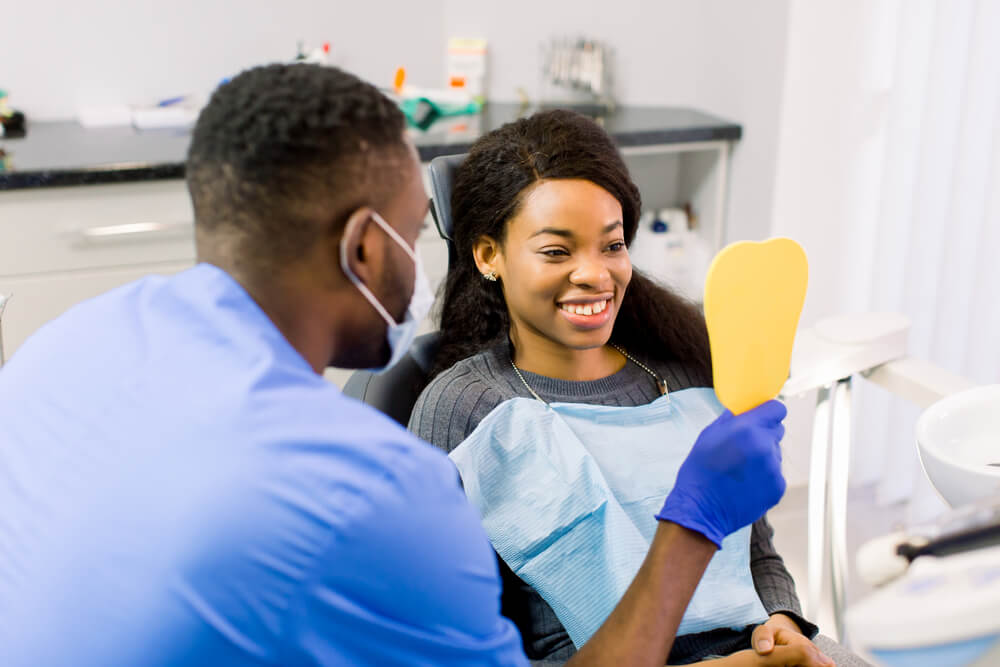 Male dentist speaking with patient in dental clinic and shows her teeth in the mirror