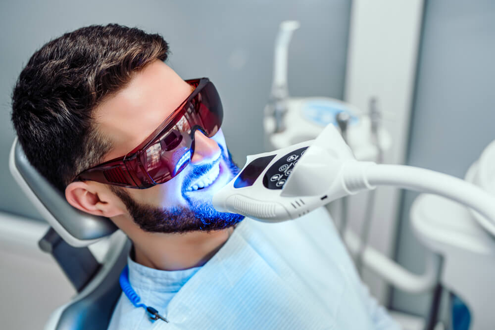 Dentist starting teeth whitening procedure with young man
