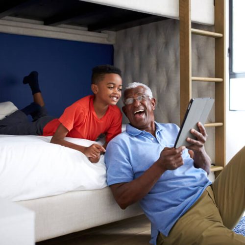 Grandfather With Grandson Lying In Bedroom Playing Game On Digital Tablet Together